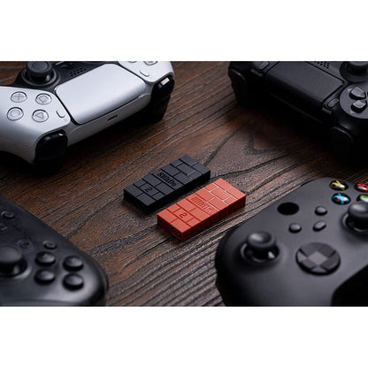 Flat lay of 8Bitdo USB Wireless Adapter 2 in red and black alongside various gaming controllers.