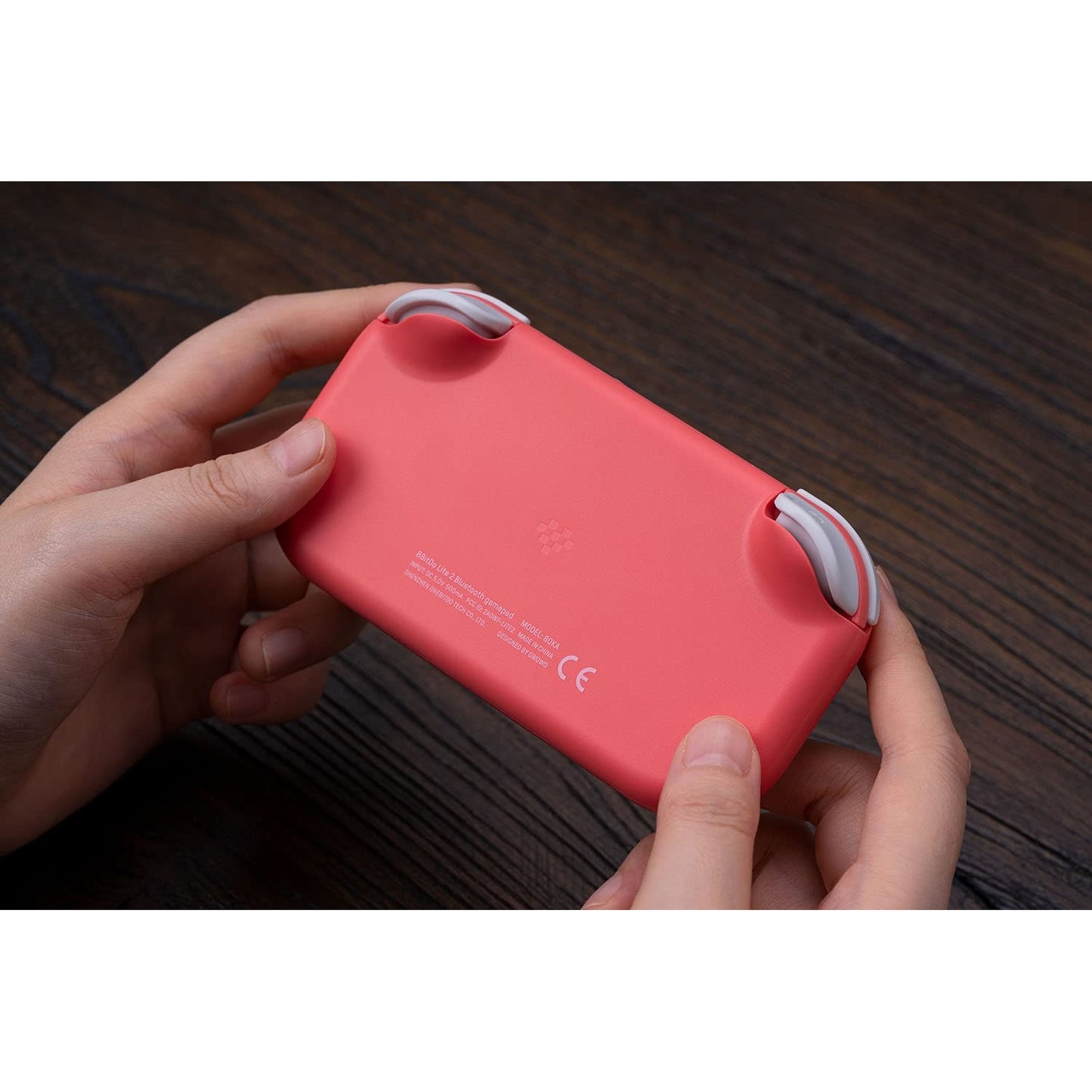 Back view of 8BitDo Lite 2 pink controller being held, showing rear design and product markings.